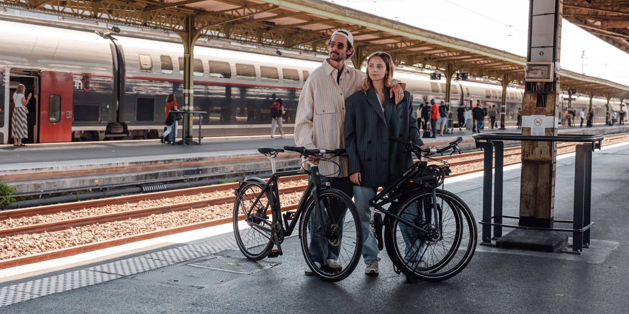 Un couple sur un quai de gare avec un bastille électrique plié et un bastille électrique déplié.