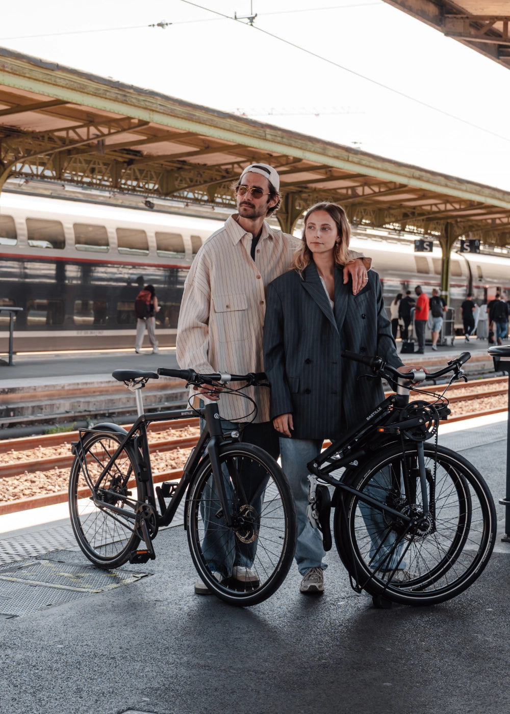 Un couple sur un quai de gare avec un bastille électrique plié et un bastille électrique déplié.